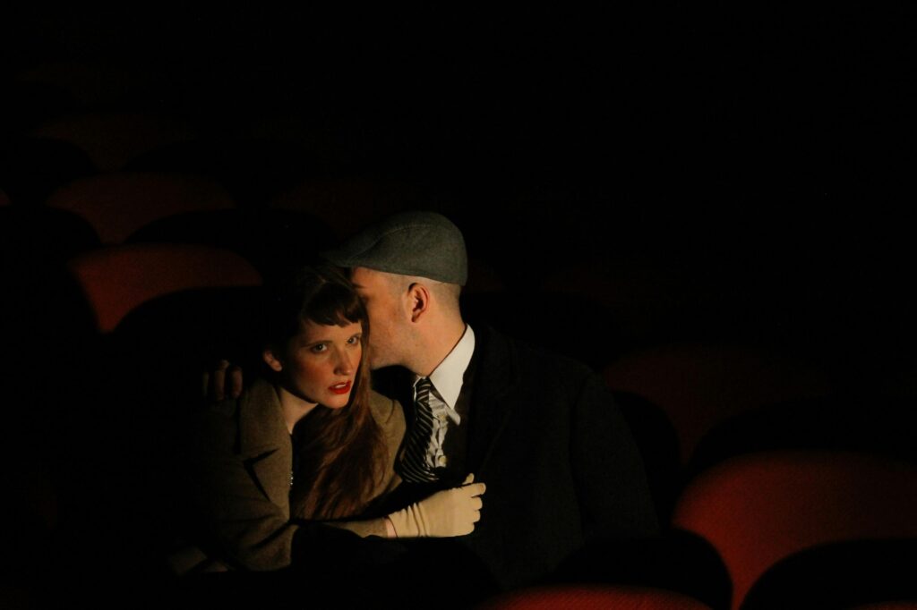 man and woman whispering in a cinema. Oldfashioned decor. Picture by Catalina Chiaravalla via Pexels