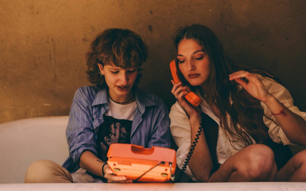 two girls sitting on the bed receiving a phonecall. This image illustrates a love scene where two people ar eabout to get it on, but they are interrupted.