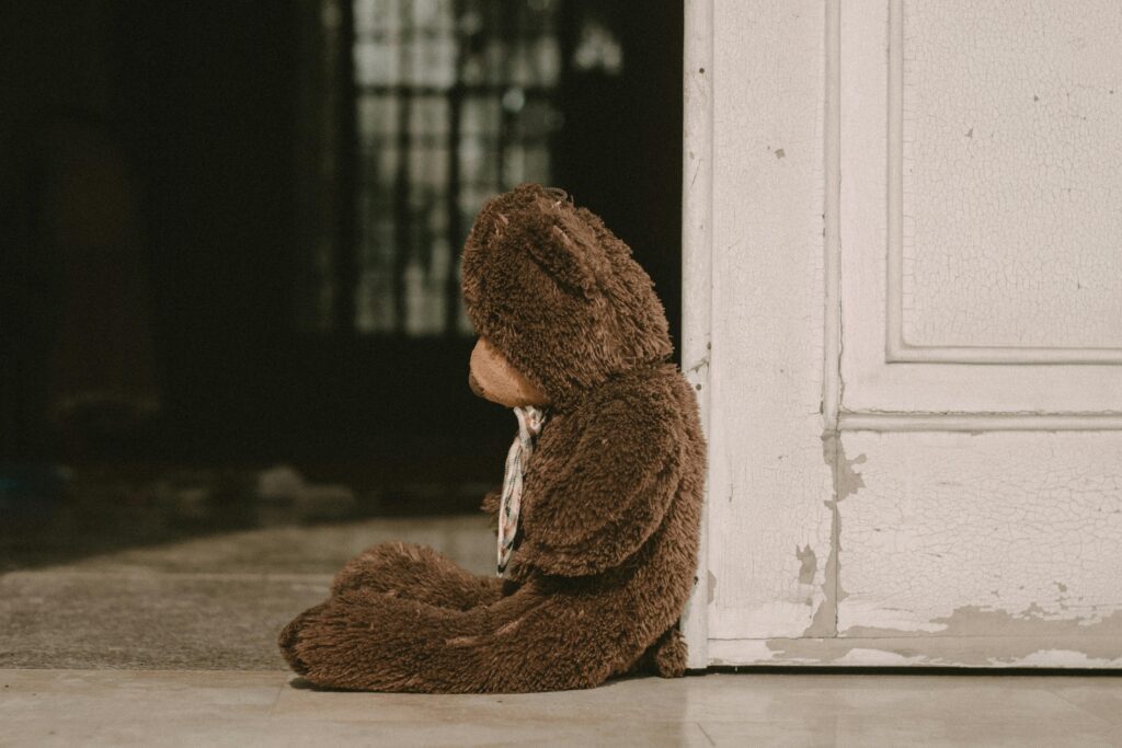 Picture of a big brown teddy bear leaning against a door, giving a nostalgic atmosphere. photo by jlimproject via Pexels